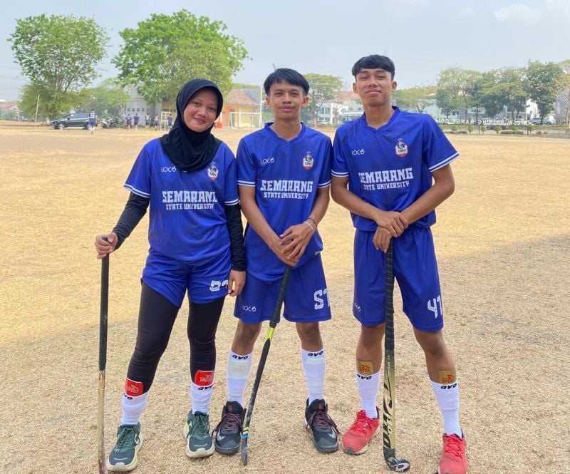 Dian Eka Wulandari, Muhamad Almaas Atha Hilal, and Muhamad Yuliyanto on the UNESA hockey field. 