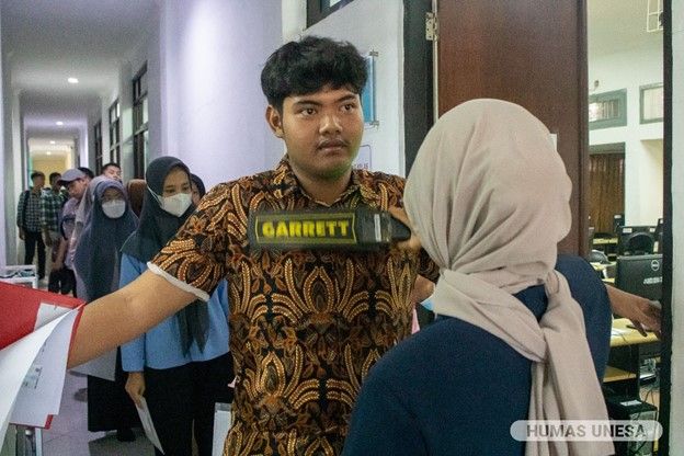 The supervisor checks and ensures that the participants are clean from prohibited items during the UTBK test using a metal detector.